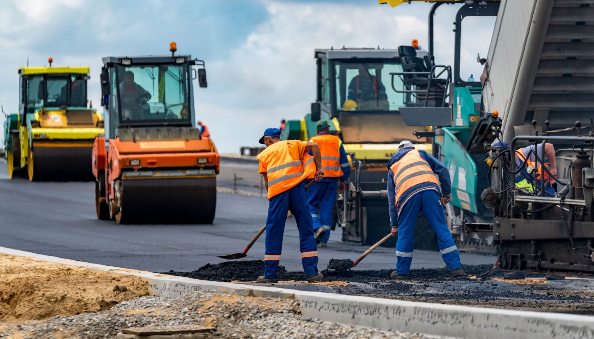 A group of construction workers wearing hard hats and reflective vests, operating heavy machinery and laying down asphalt on a newly excavated road in Phoenix, showcasing the intricate process of building a sturdy and smooth surface.