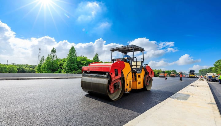 A team of construction workers operating heavy machinery, meticulously laying down fresh, smooth asphalt on a newly constructed road in Phoenix, with steam rising from the hot surface.